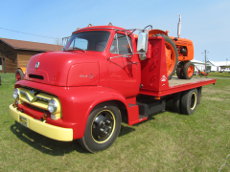 Ford C600 flatbed truck hauling a COOP tractor.