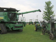 New John Deere combine next to a John Deere threshing machine.